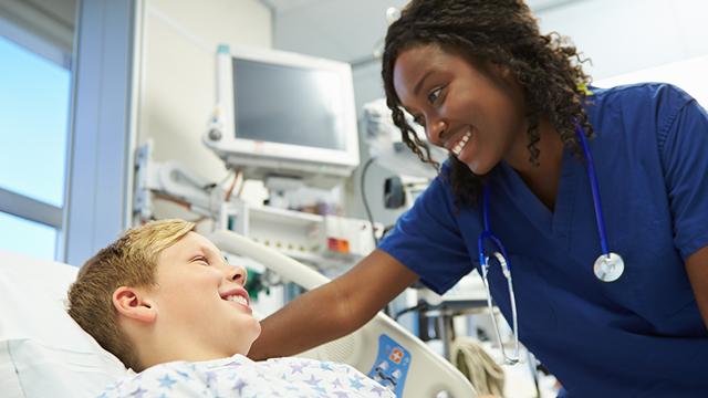 一个穿着蓝色手术服的护士对着病床上的小男孩微笑.
